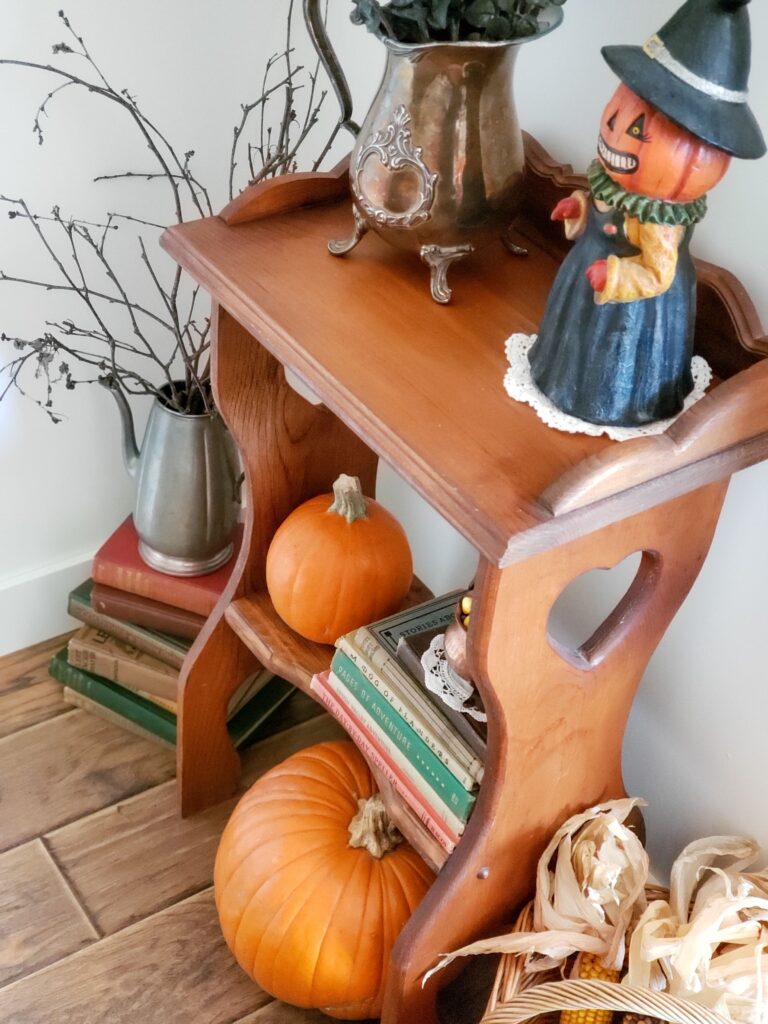 vintage fall vignette with pumpkins, an old table with stack of books, a witch figurine, and vases with branches