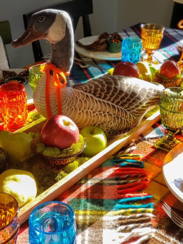 vintage thanksgiving tablescape with plush goose, colored glassware, plaid blankets, apples and pears.