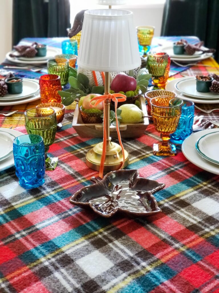 vintage thanksgiving tablescape with plush goose, colored glassware, plaid blankets, apples and pears.