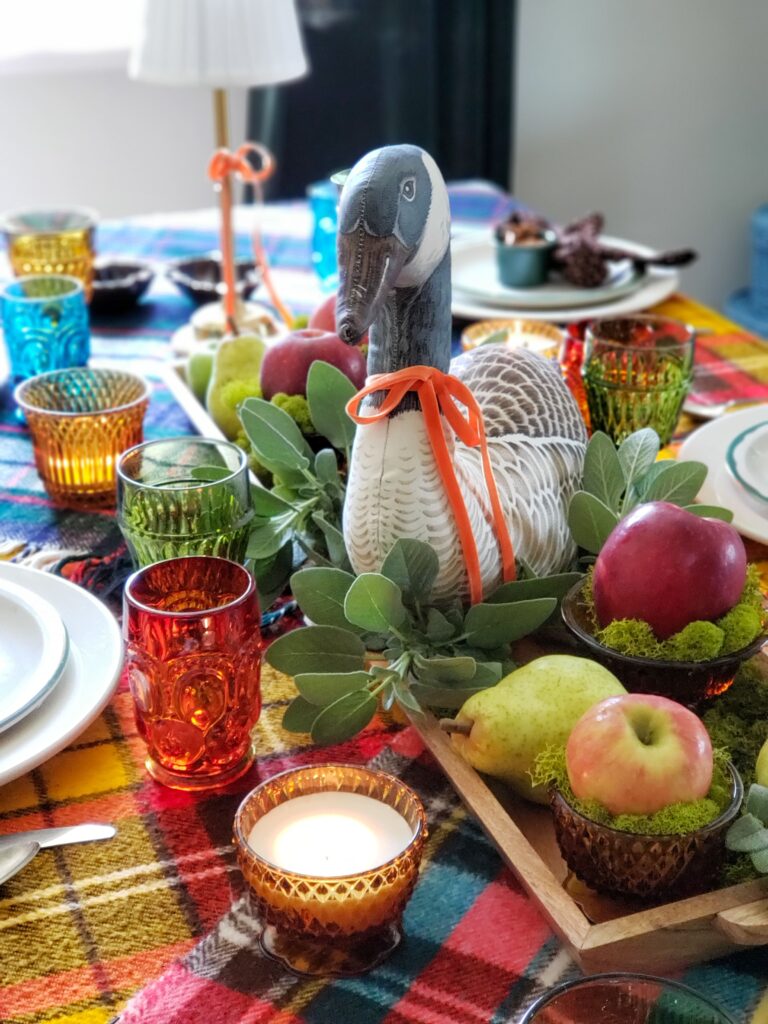 vintage thanksgiving tablescape with plush goose, colored glassware, plaid blankets, apples and pears.