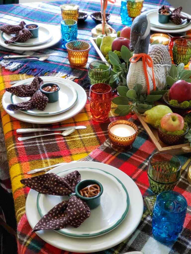 vintage thanksgiving tablescape with plush goose, colored glassware, plaid blankets, apples and pears.