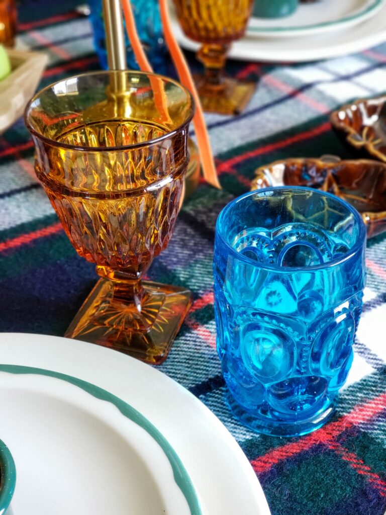 vintage thanksgiving tablescape with plush goose, colored glassware, plaid blankets, apples and pears.