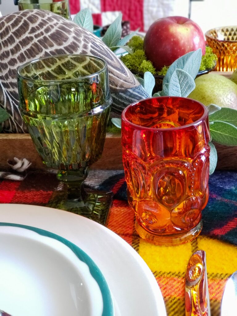vintage thanksgiving tablescape with plush goose, colored glassware, plaid blankets, apples and pears.