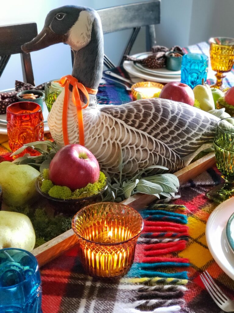 vintage thanksgiving tablescape with plush goose, colored glassware, plaid blankets, apples and pears.