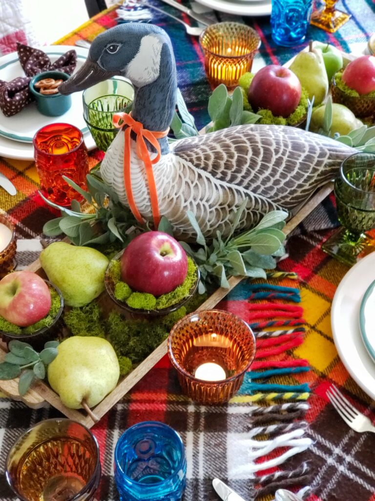 vintage thanksgiving tablescape with plush goose, colored glassware, plaid blankets, apples and pears.