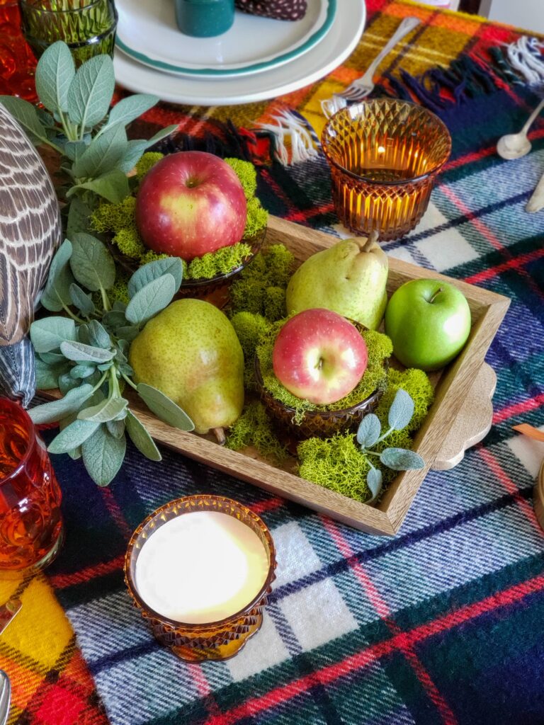 vintage thanksgiving tablescape with plush goose, colored glassware, plaid blankets, apples and pears.