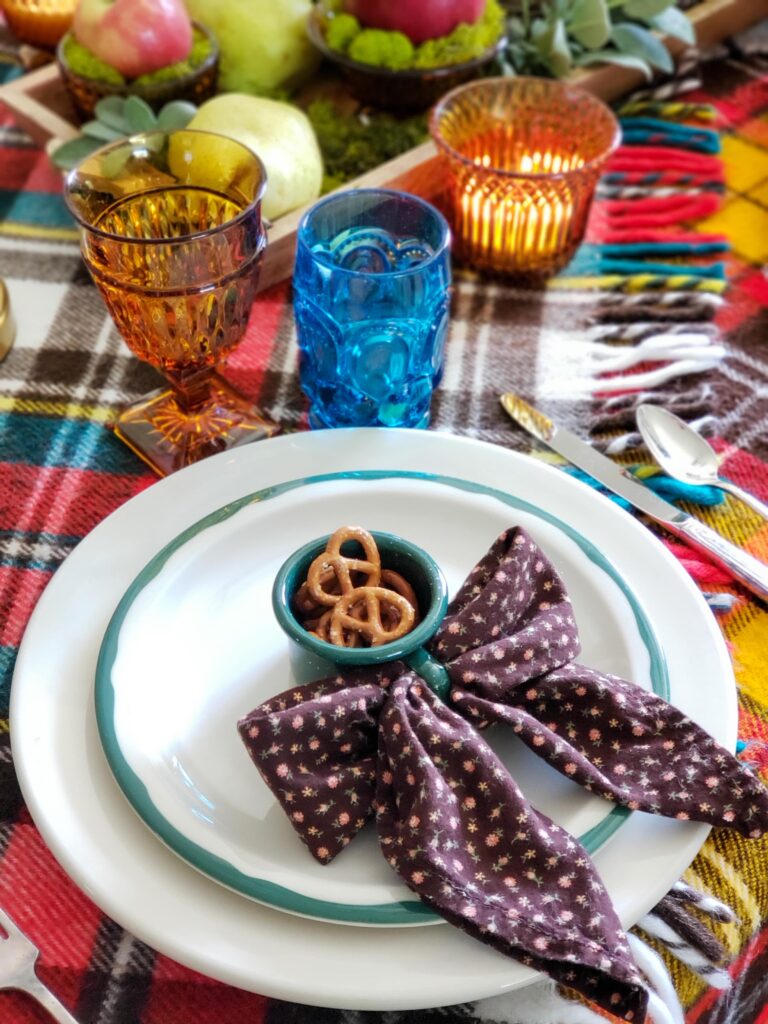 vintage thanksgiving tablescape with plush goose, colored glassware, plaid blankets, apples and pears.