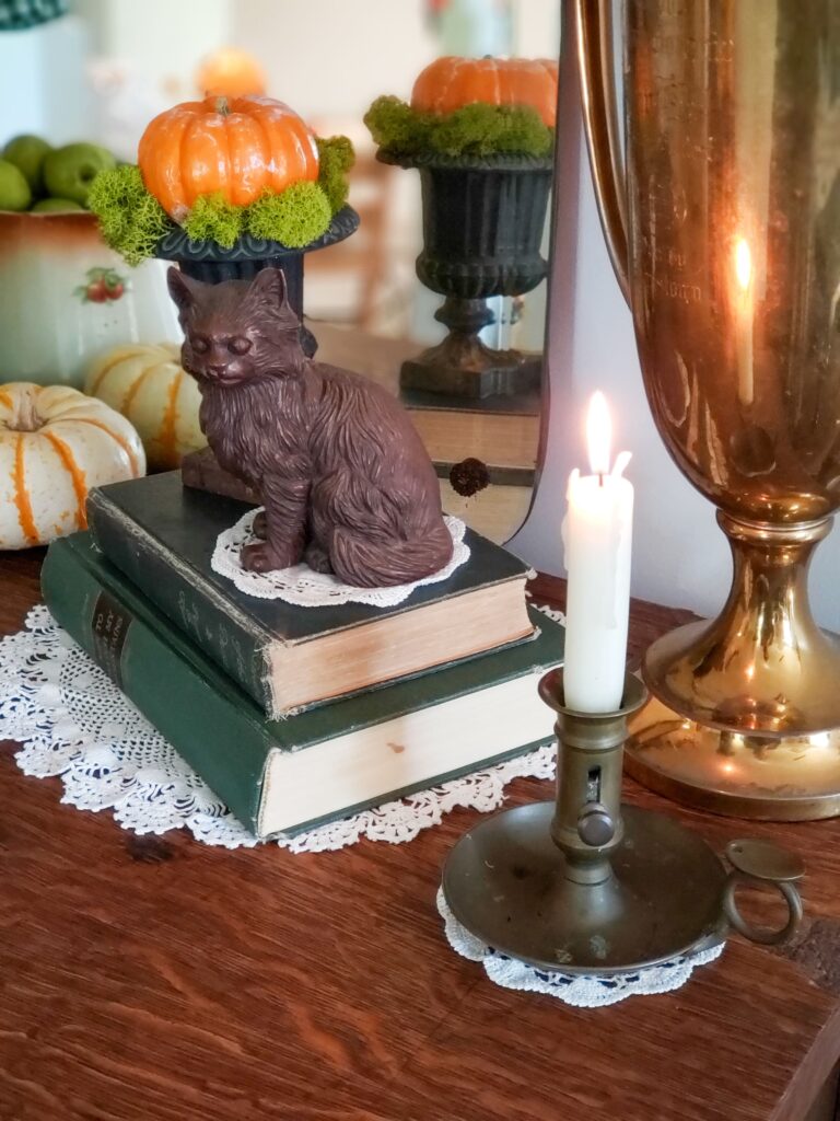 cozy cottage halloween decor with books, vintage pitcher, pumpkins, teacups a mirror and cat.