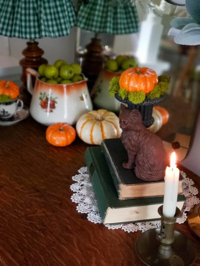 cozy cottage halloween decor with books, vintage pitcher, pumpkins, teacups a mirror and cat.