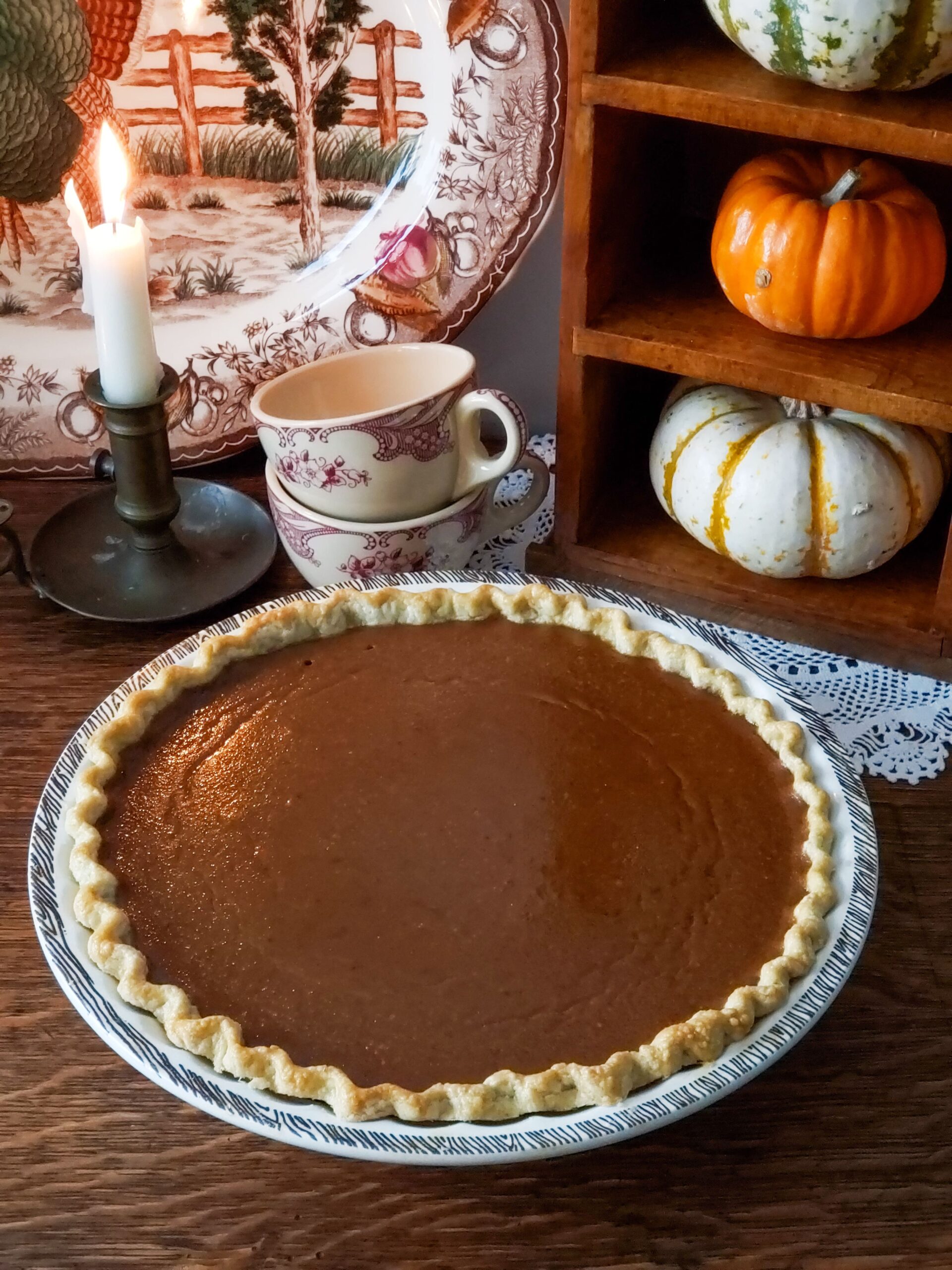 old fashioned pumpkin pie with candle cups and turkey platter in the background