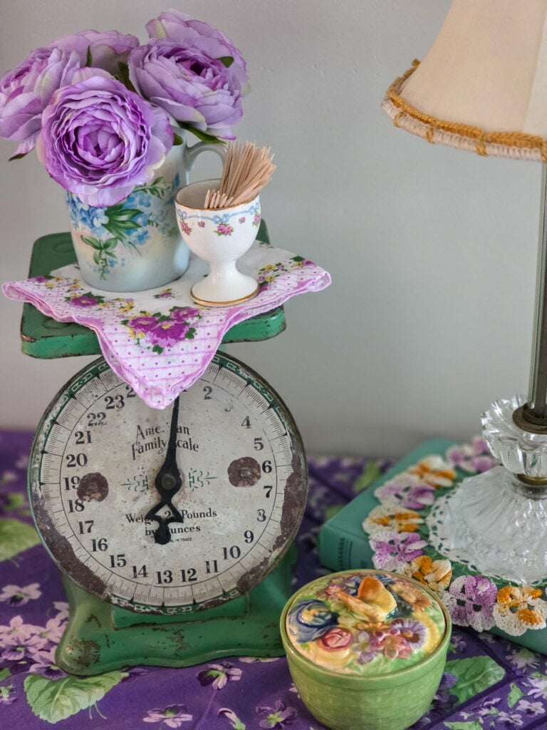a green scale with hanky and vintage mug on top filled with purple flowers