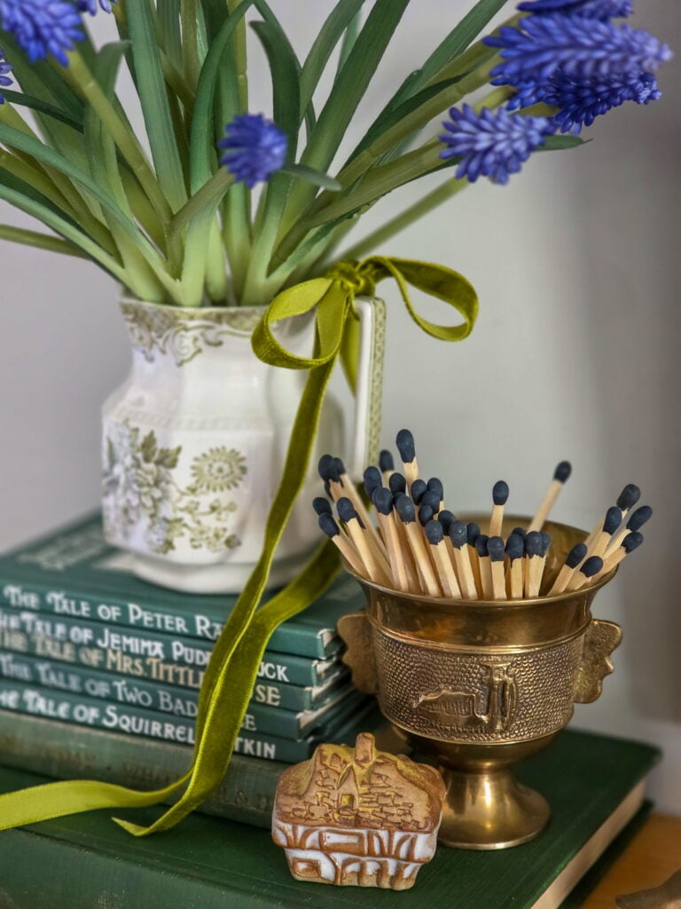 vintage creamer with flowers on top of books, a brass item holding matches and a small cottage object