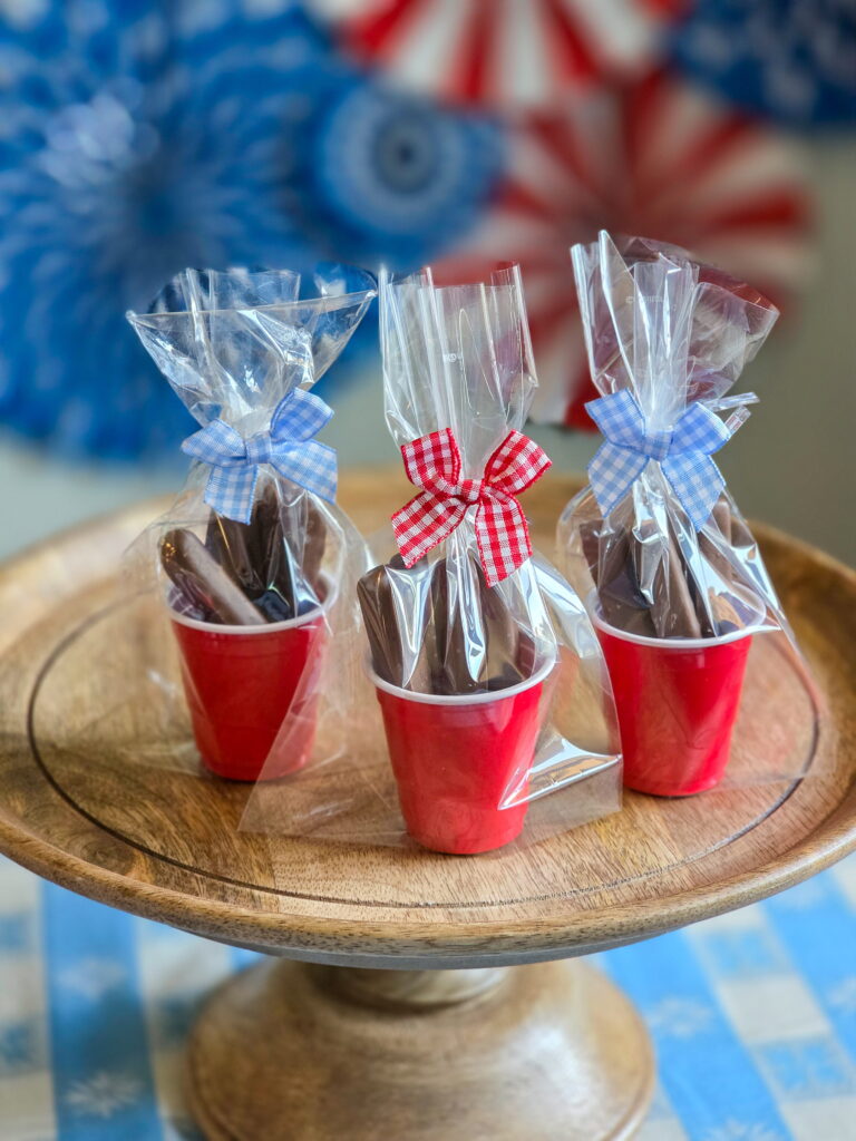 DIY vintage Americana party favor with chocolate raspberry sticks in mini red cups and gingham bow sitting on a wood cake stand
