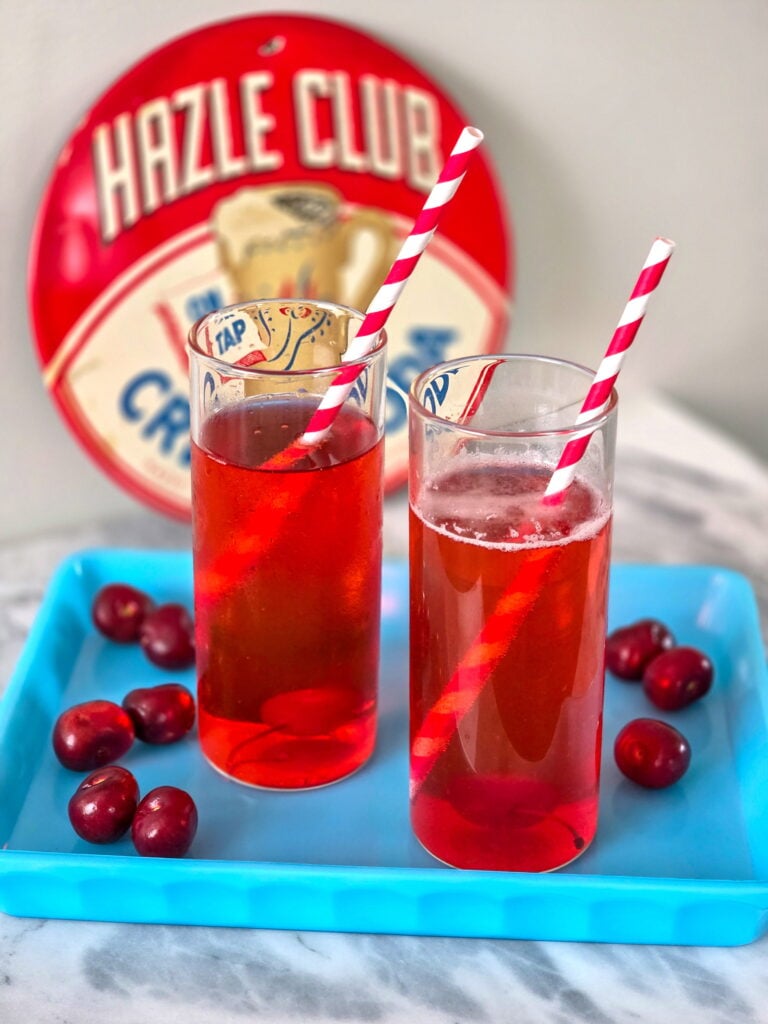 old-fashioned cherry phosphate recipe in tall glass with retro straws sitting on a blue tray with cherries.