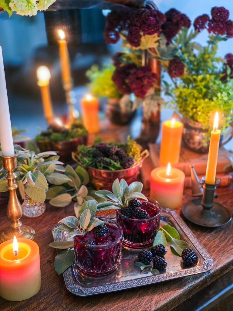 gillian owens blackberry bourbon cocktail with sage garnish sitting on vintage silver tray with blackberries and warm candles lit