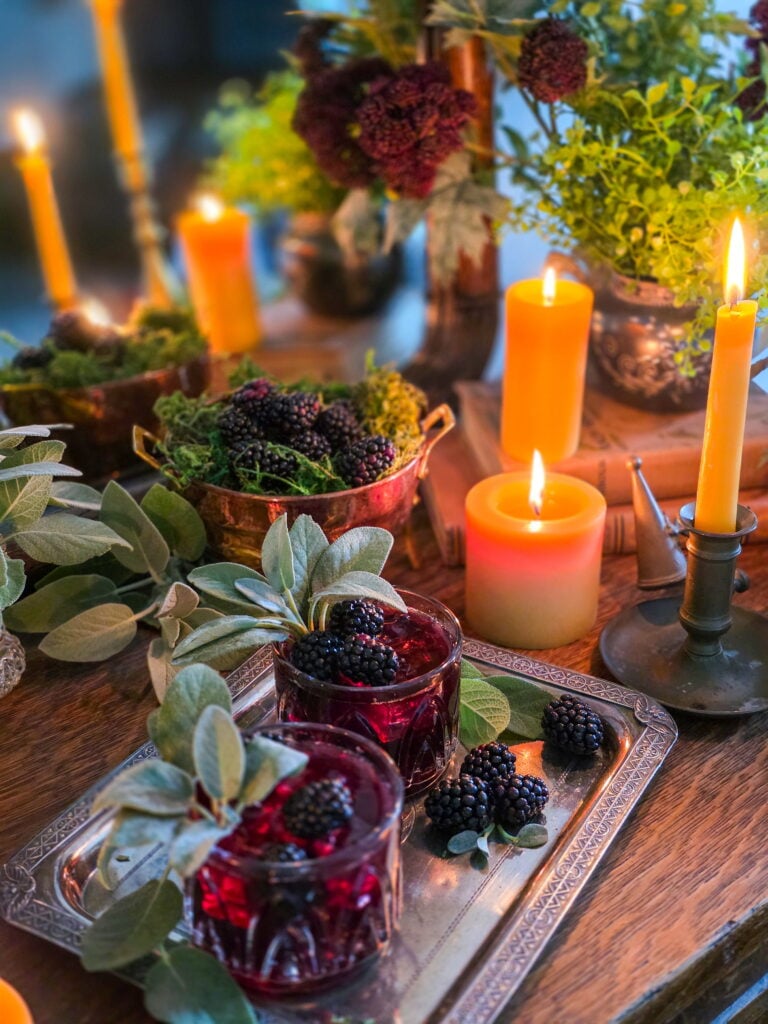 gillian owens blackberry bourbon cocktail with sage garnish sitting on vintage silver tray with blackberries and warm candles lit
