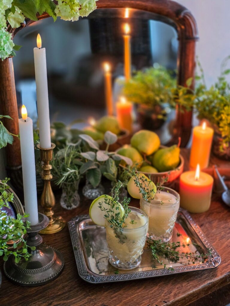 gin pear cocktail in vintage glass with thyme sprig garnish, and lit candles and a bowl of pears