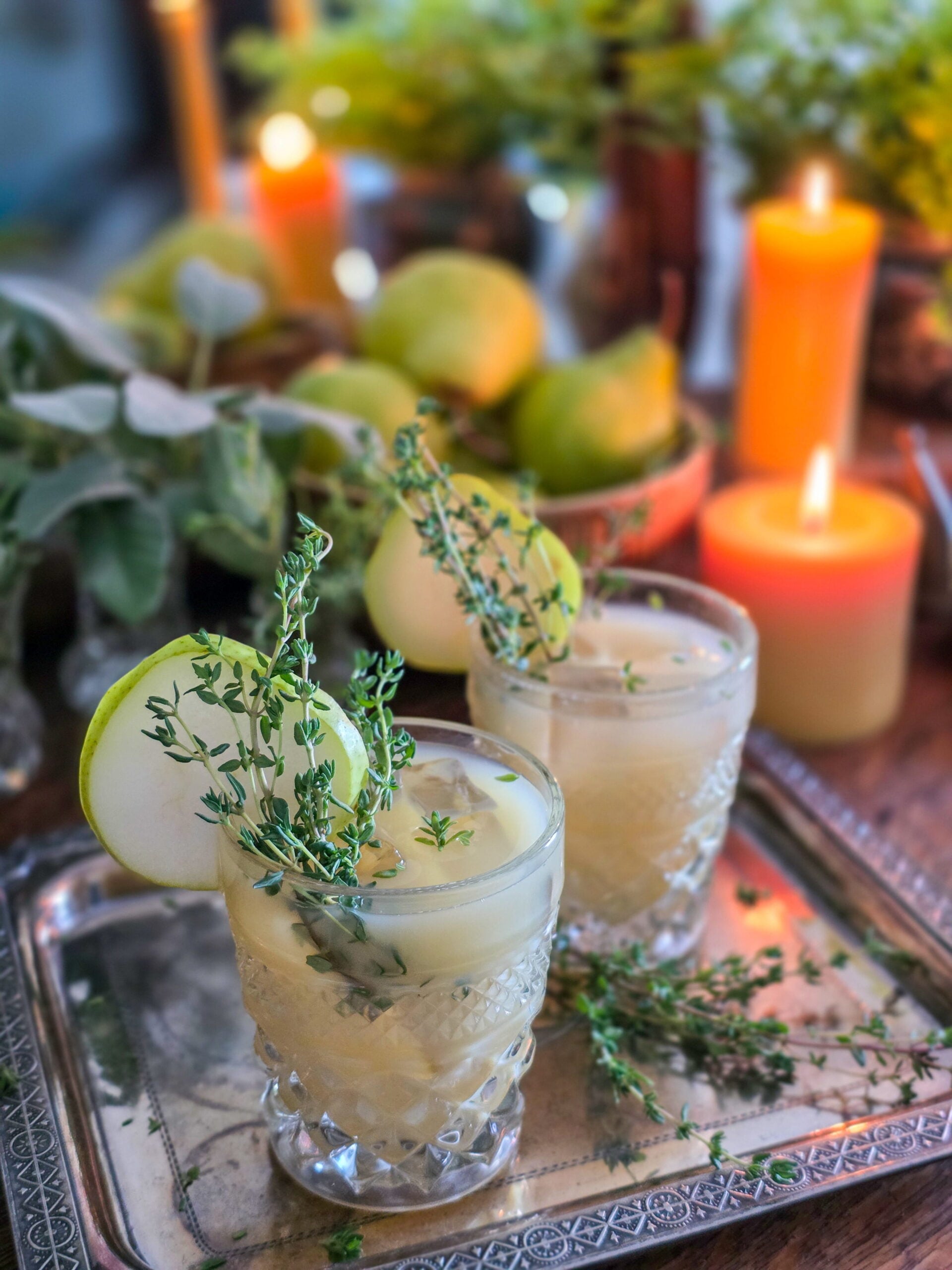 gin pear cocktail in vintage glass with thyme sprig garnish, and lit candles and a bowl of pears
